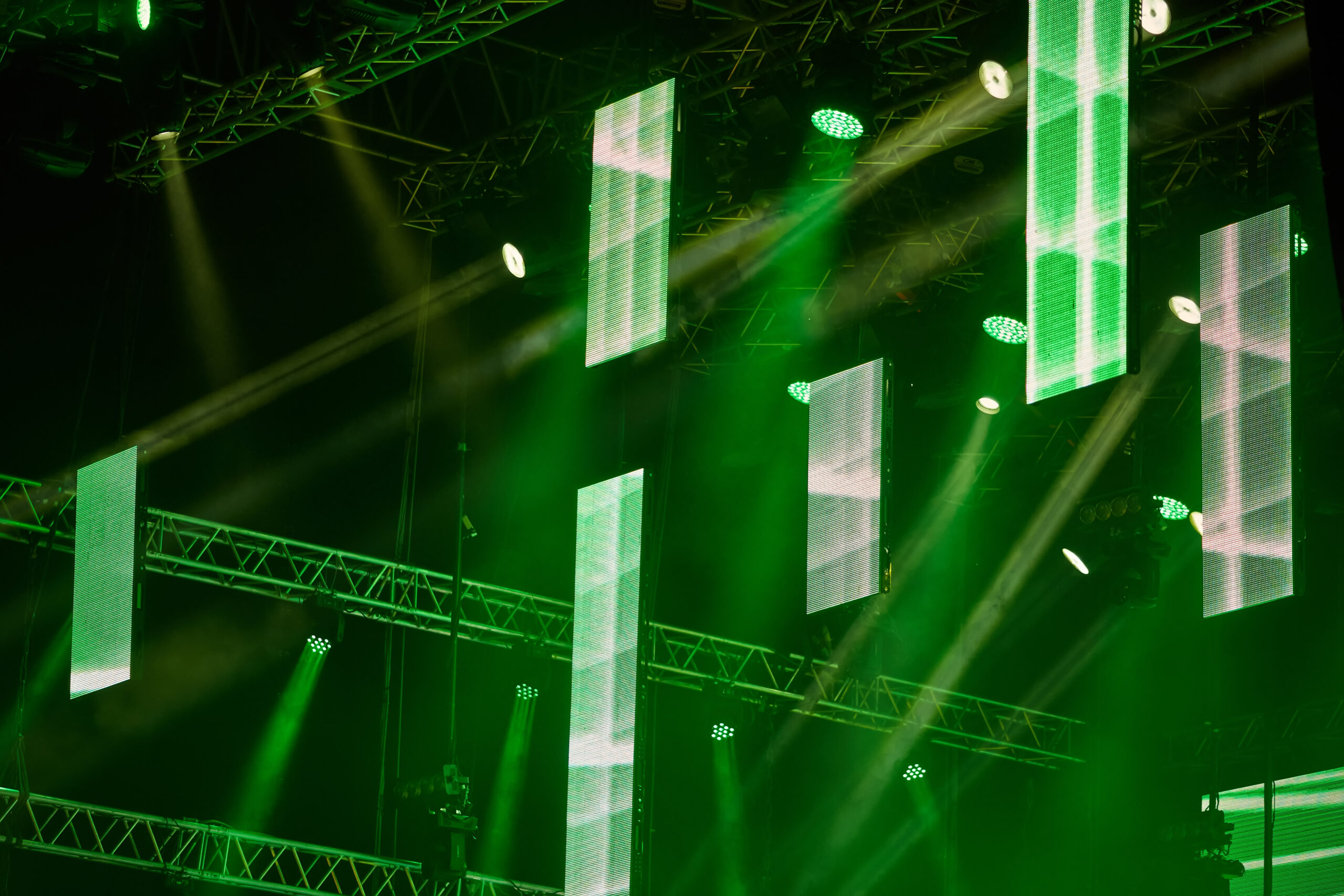Professional stage scenography designed by YMVRSL in Ankara, Turkey, featuring extensive aluminum trusses, synchronized green LED spotlights, and multiple vertically suspended digital LED video screen strips.